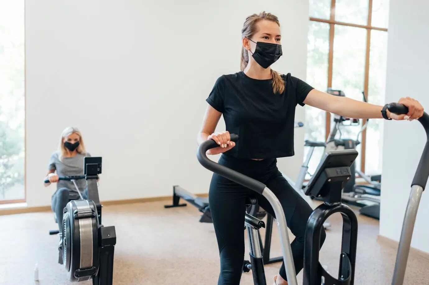 Women exercise at a gym while wearing medical masks during the pandemic.